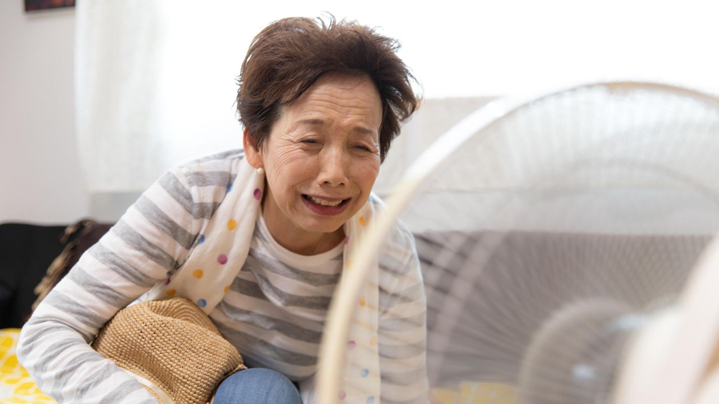 Eine ältere Dame kühlt sich vor einem Ventilator ab