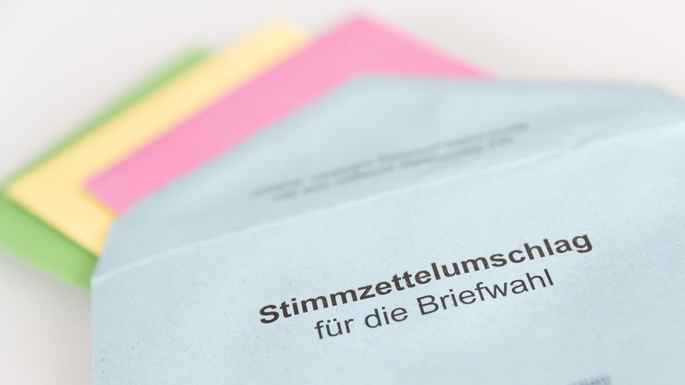 Auf einem weißen Tisch liegt ein blauer Briefumschlag mit dem Aufdruck "Stimmzettelumschlag für die Briefwahl"