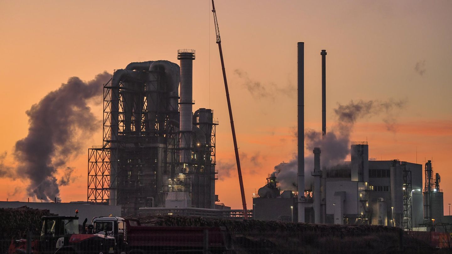 Industrieanlage mit dampfenden Schornsteinen vor rot schimmerndem Himmel