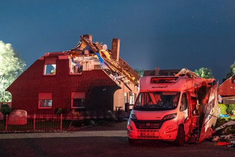 Vor einem durch einen Sturm beschädigten Haus steht ein Wohnmobil, dessen Aufbau an der Seite aufgerissen ist