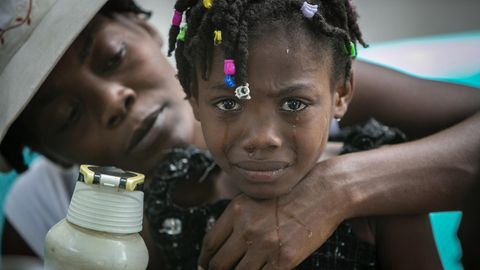 Einem farbigen Mädchen mit bunten Perlen in den Dreads laufen Tränen über das Gesicht, während eine Frau es von hinten umarmt