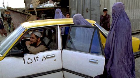 Afghanistan: Zwei Frauen in hellblauen Burkas steigen hinten in ein weiß-gelbes Taxi auf einer Straße Kabuls ein