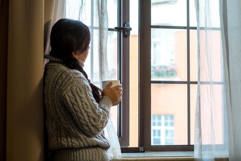 Frau hält eine Tasse und schaut aus dem Fenster