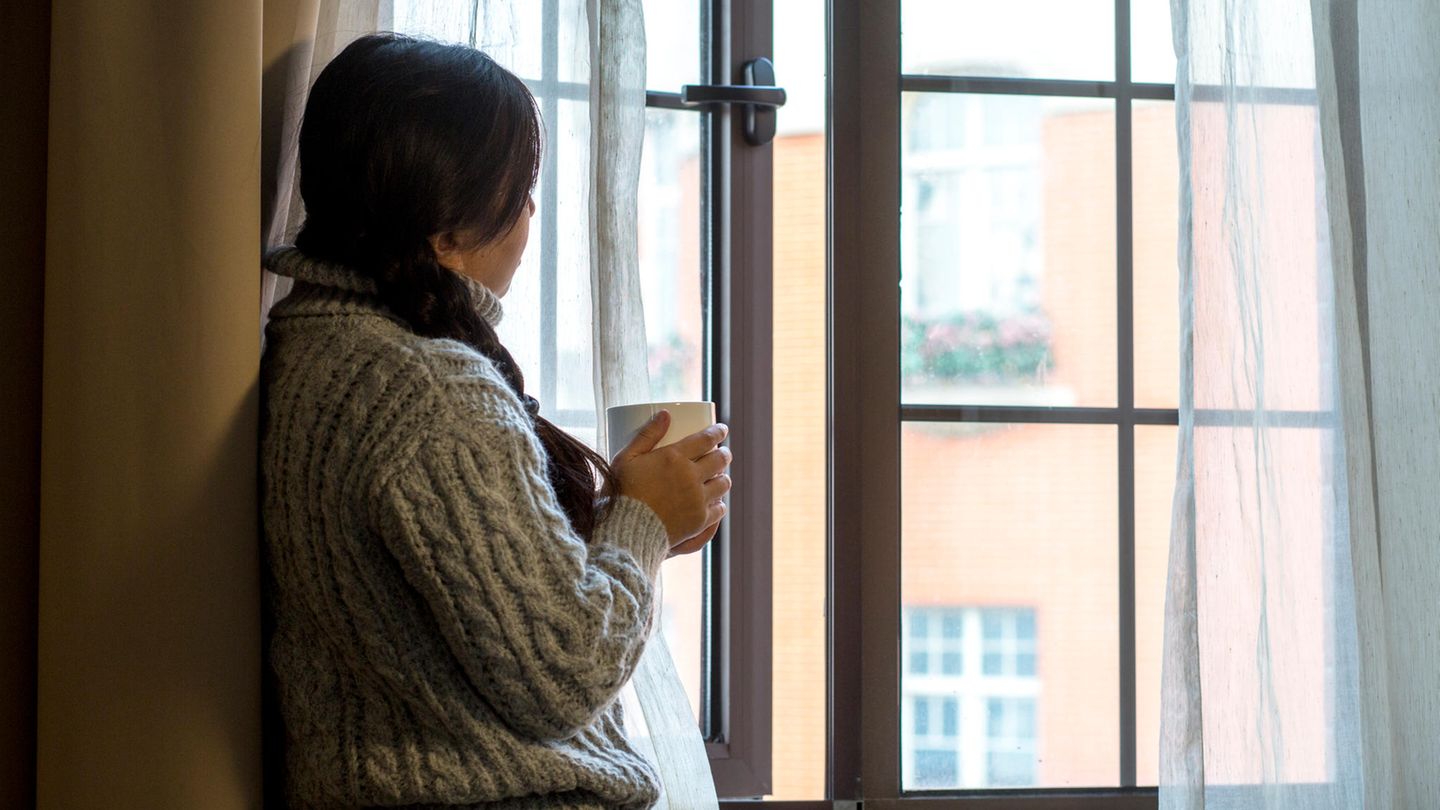 Frau hält eine Tasse und schaut aus dem Fenster
