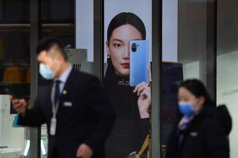Menschen in Beijing gehen an einer Werbung für Smartphones vorbei