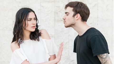Junge Frau schiebt jungen Mann angeekelt beiseite. Er versucht gerade sie zu küssen.