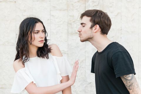 Junge Frau schiebt jungen Mann angeekelt beiseite. Er versucht gerade sie zu küssen.