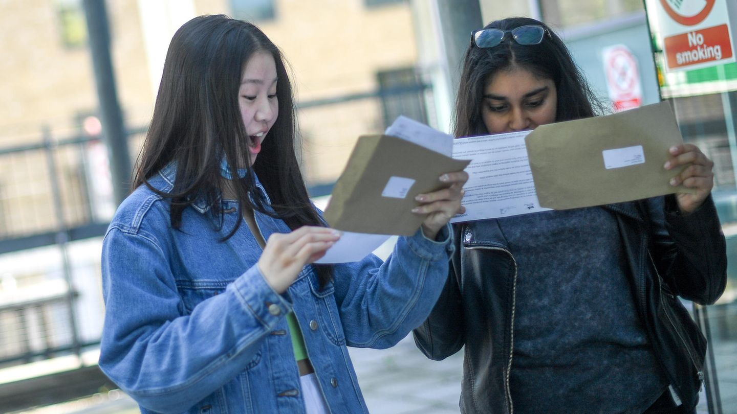 Zwei Studentinnen schauen in Briefumschläge, eine freut sich, eine nicht