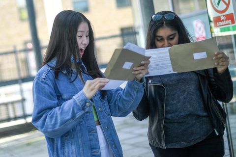 Zwei Studentinnen schauen in Briefumschläge, eine freut sich, eine nicht