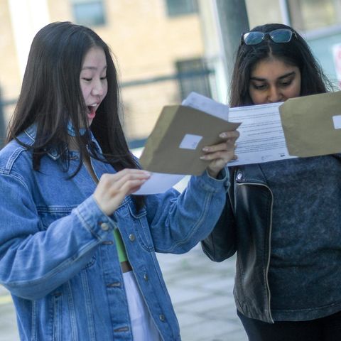 Zwei Studentinnen schauen in Briefumschläge, eine freut sich, eine nicht