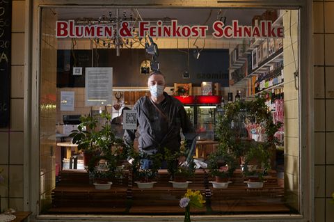 Uwe Schnalke trägt eine Mund-Nasen-Bedeckung und sieht durch das Schaufenster seines Ladens