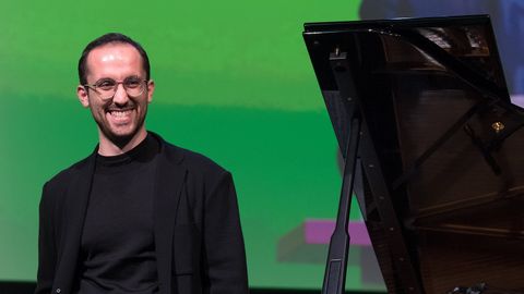 Der Pianist Igor Levit lächelt vor einem grünen Hintergrund