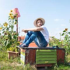 Ein junger Mann sitzt im Garten, er sieht nachdenklich aus