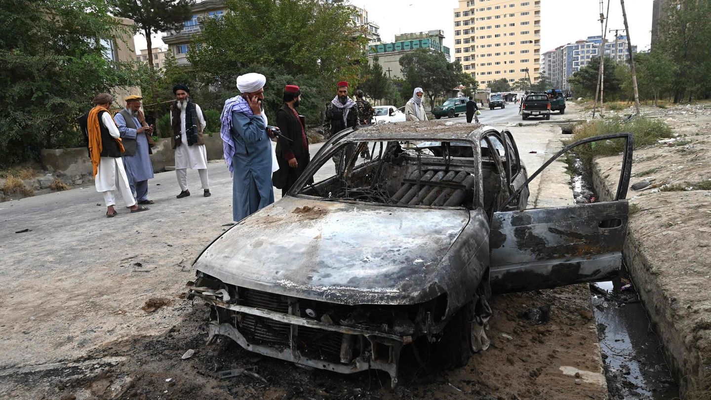 Taliban-Kämpfer stehen in Kabul neben dem ausgebranntem Wrack eines Autos