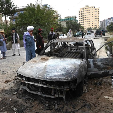 Taliban-Kämpfer stehen in Kabul neben dem ausgebranntem Wrack eines Autos
