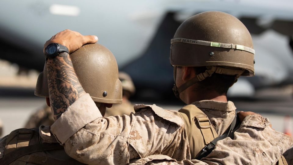 Von hinten sind zwei Soldaten in Tarnfleck und mit Helmen zu sehen. Einer legt dem anderen eine Hand auf den Helm