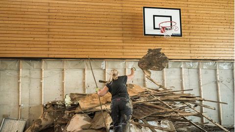 Unter dem Basketballkorb werfen die Eltern die vom Hochwasser zerstoert Einrichtung auf einen Haufen