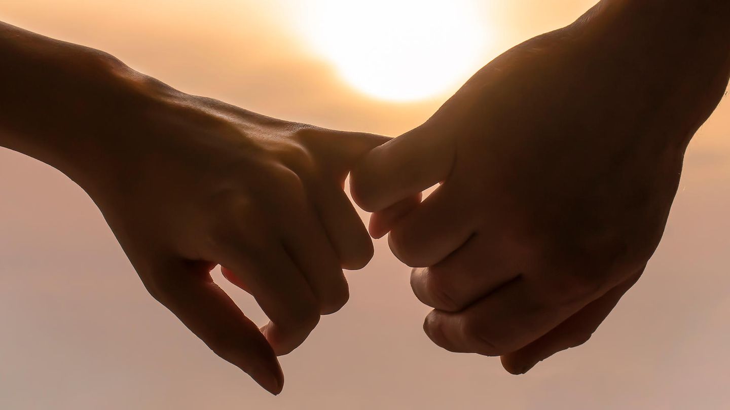 Zwei Hände halten sich an den Fingern im Sonnenuntergang