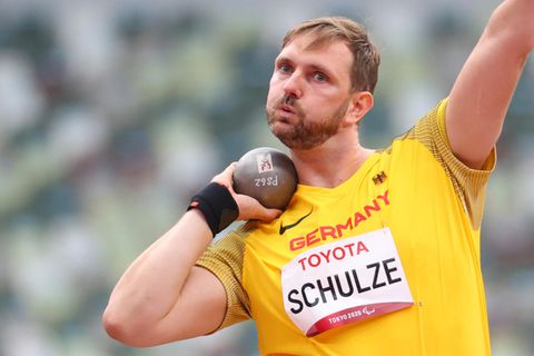 Ein weißer Mann mit dunkelblondem Seitenscheitel und Vollbart setzt mit der rechten Hand zum Kugelstoßen an