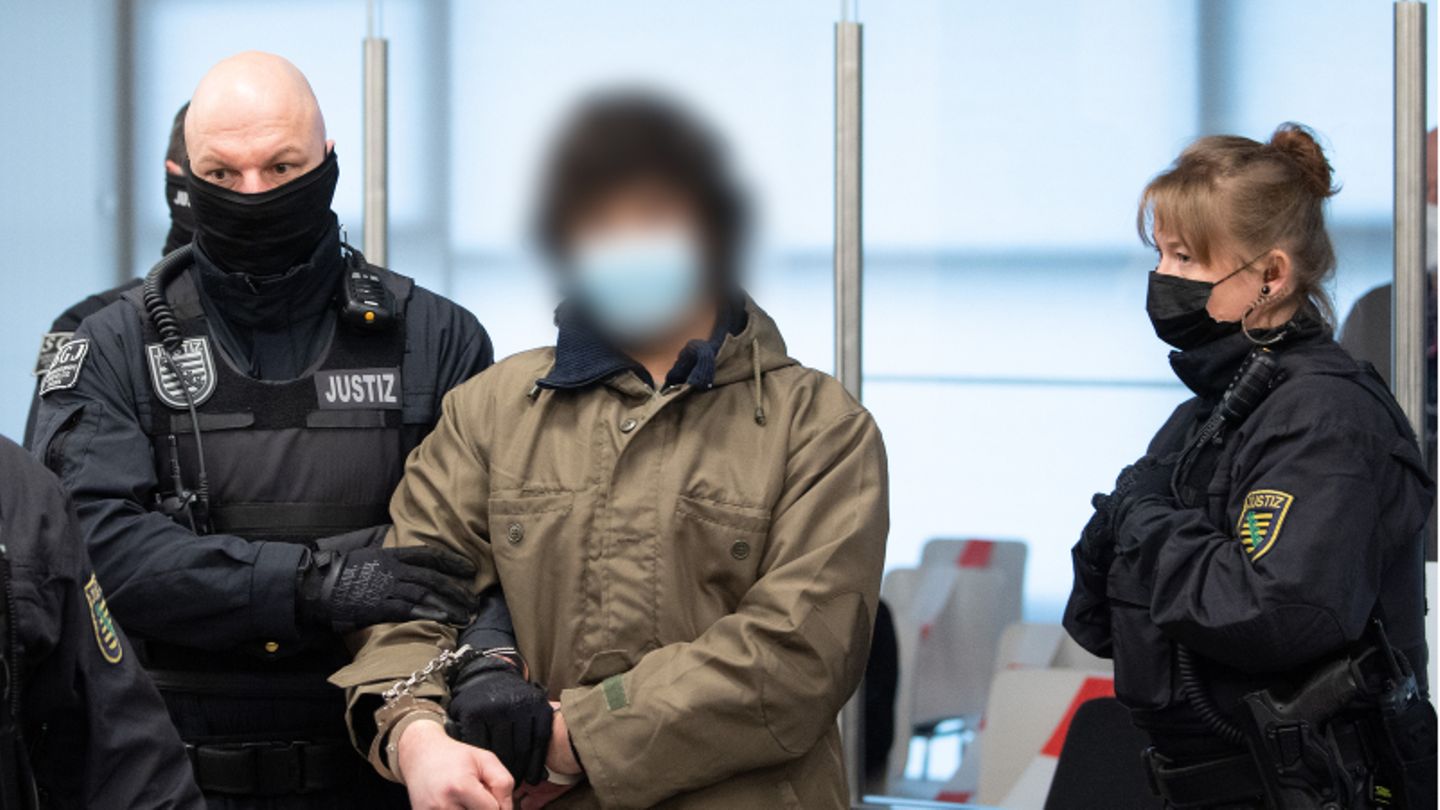 Ein Angeklagter wird vor Prozessbeginn von Justizbeamten in den Verhandlungssaal geführt