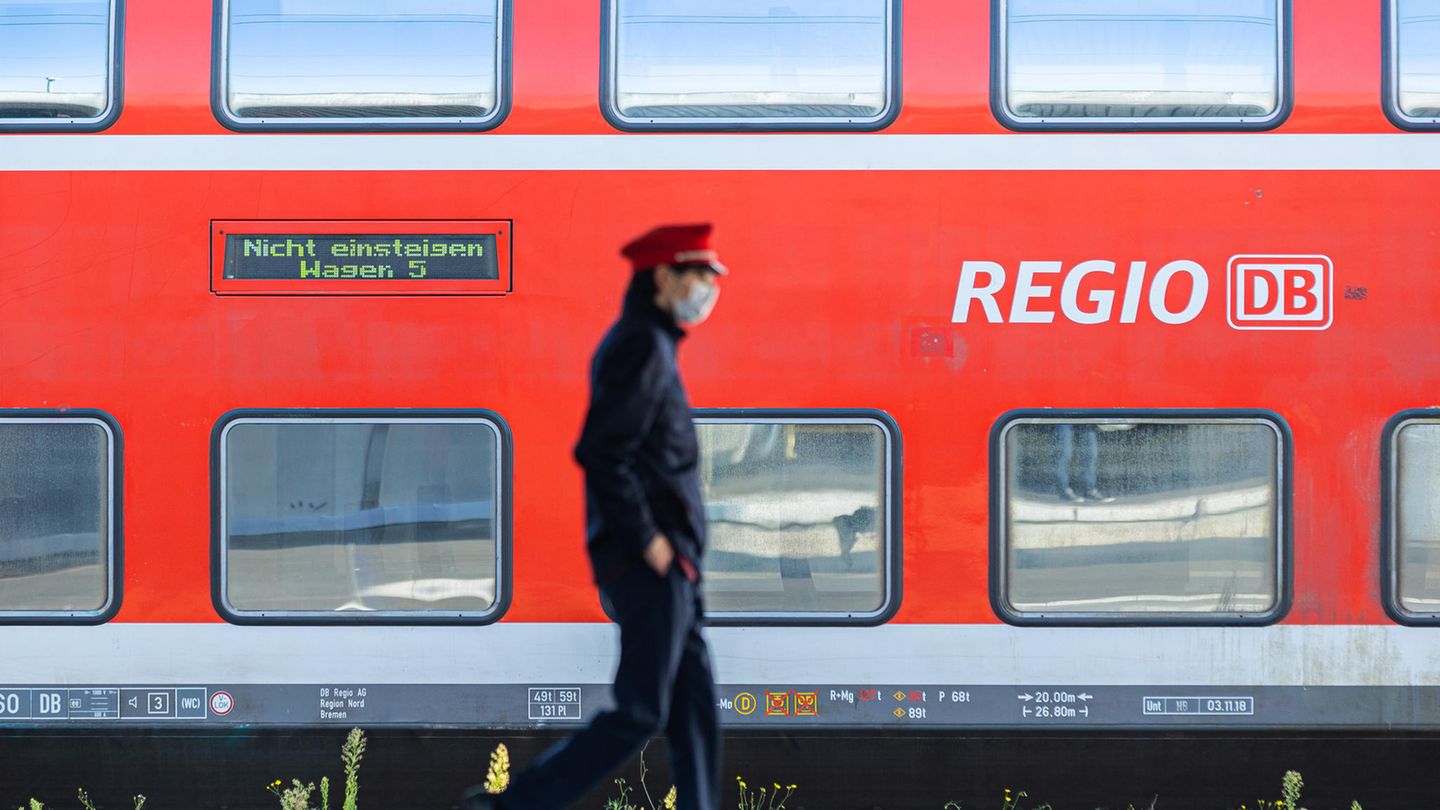 Ein Mitarbeiter der Deutschen Bahn (DB) läuft auf einem Bahnsteig und ein Zug der DB Regio steht auf einem Gleis dahinter