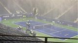 In einem leeren Tennis-Stadion mit lila Platz und grünem Außenbereich fällt Starkregen