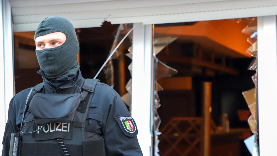 Ein Polizist steht mit Sturmhaube vor den zerborstenen Fenstern eines Vereinsheims der Hells Angels in Mönchengladbach
