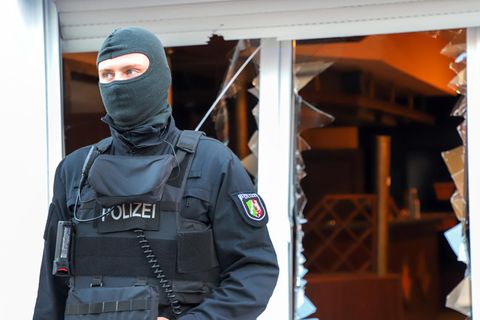 Ein Polizist steht mit Sturmhaube vor den zerborstenen Fenstern eines Vereinsheims der Hells Angels in Mönchengladbach