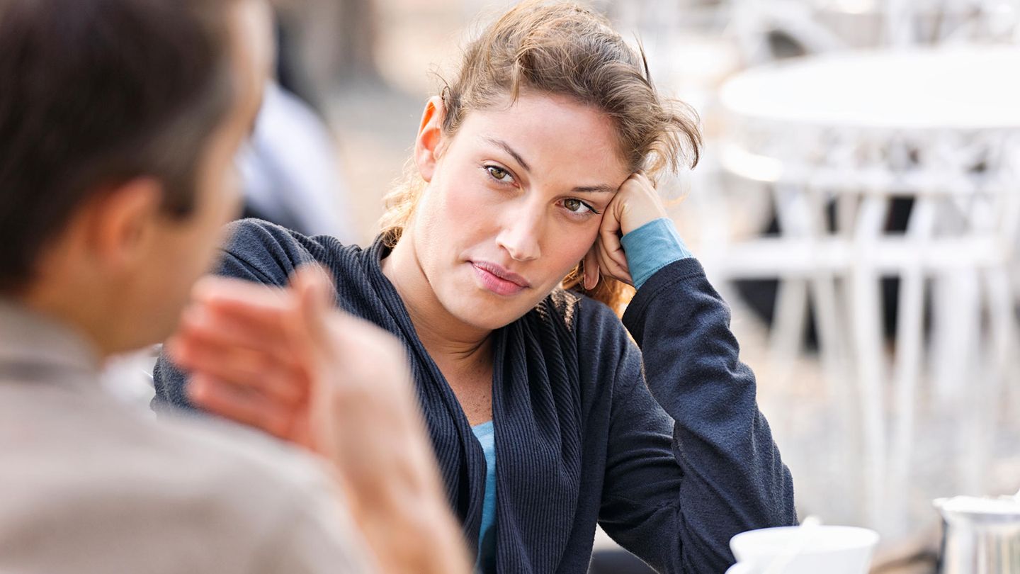 Frau und Mann unterhalten sich in einem Café, Frau schaut skeptisch