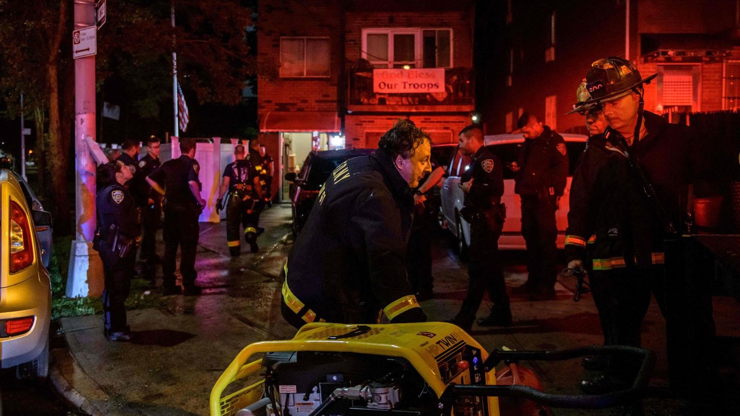 Ein Feuerwehrmann in Uniform beugt sich über eine Motorpumpe mit gelbem Schutzrahmen, ein zweiter schaut ihn an