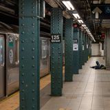 Während eine silbern glänzende Metro im Gleis steht, schläft ein Mann auf dem Bahnsteig mit Rucksack als Kopfkissen