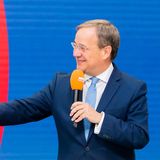 Zwei weiße Männer in Anzügen begrüßen sich auf einem Podium Faust an Faust