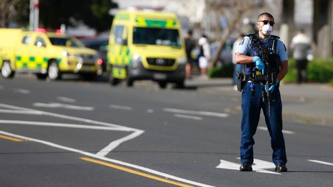 Ein Polizist steht mit Sturmgewehr auf einer Straße, während im Hintergrund gelbe Rettungswagen stehen