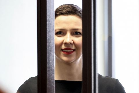 Eine weiße Frau mit kurzen, braunen Haaren lächelt hinter zwei dicken Gitterstäben hervor