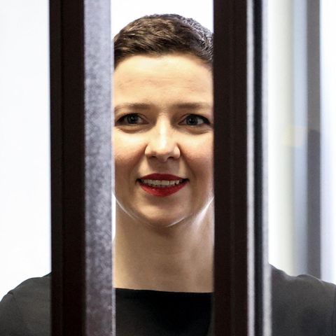 Eine weiße Frau mit kurzen, braunen Haaren lächelt hinter zwei dicken Gitterstäben hervor