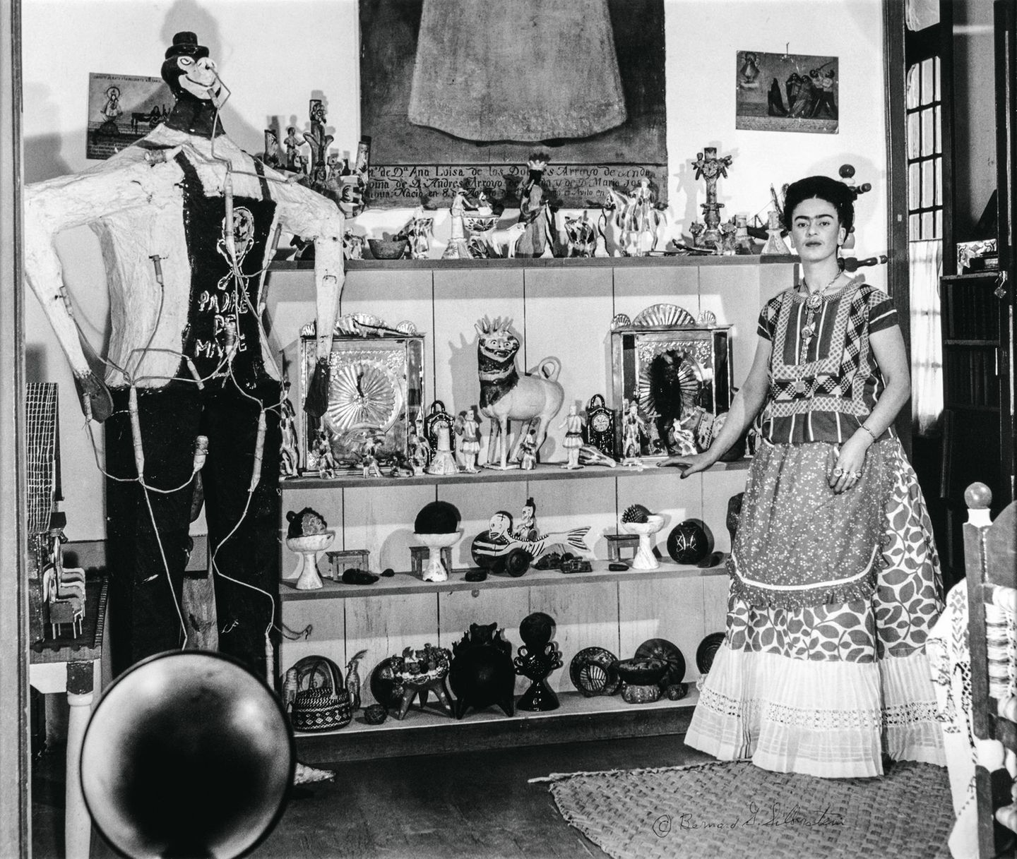 Frida Kahlo mit ihrer Sammlung von Objekten mexikanischer Volkskunst mit einer überlebensgroßen Judasfigur aus Pappmaschee im Wohnzimmer des "Blauen Hauses", um 1940