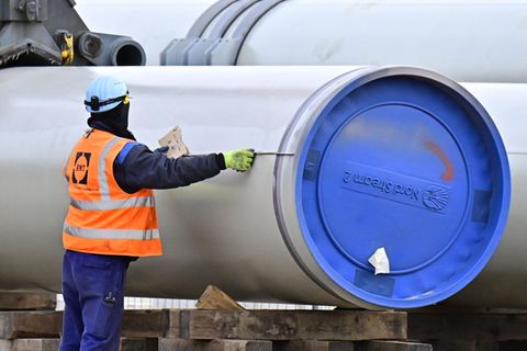 Ein Mann in blauer Arbeitskleidung und orangener Warnweste misst ein Rohr mit blauem "Nord Stream 2"-Verschluss aus