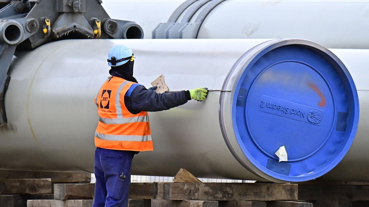 Ein Mann in blauer Arbeitskleidung und orangener Warnweste misst ein Rohr mit blauem "Nord Stream 2"-Verschluss aus