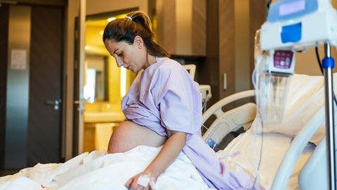 Junge Frau sitzt hochschwanger in einem Krankenhausbett
