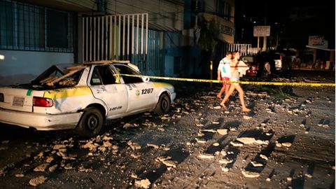 Ein Paar geht an einem Taxi vorbei, das durch herabfallende Trümmer nach einem starken Erdbeben beschädigt wurde.