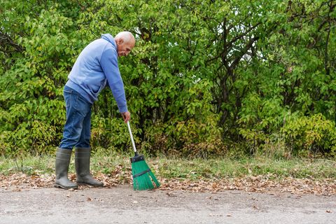 Ein älterer Mann fegt Laub auf der Straße