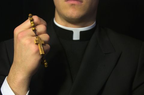Ein katholischer Geistlicher hält einen Rosenkranz mit Kreuz