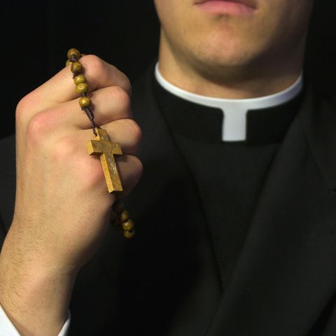 Ein katholischer Geistlicher hält einen Rosenkranz mit Kreuz