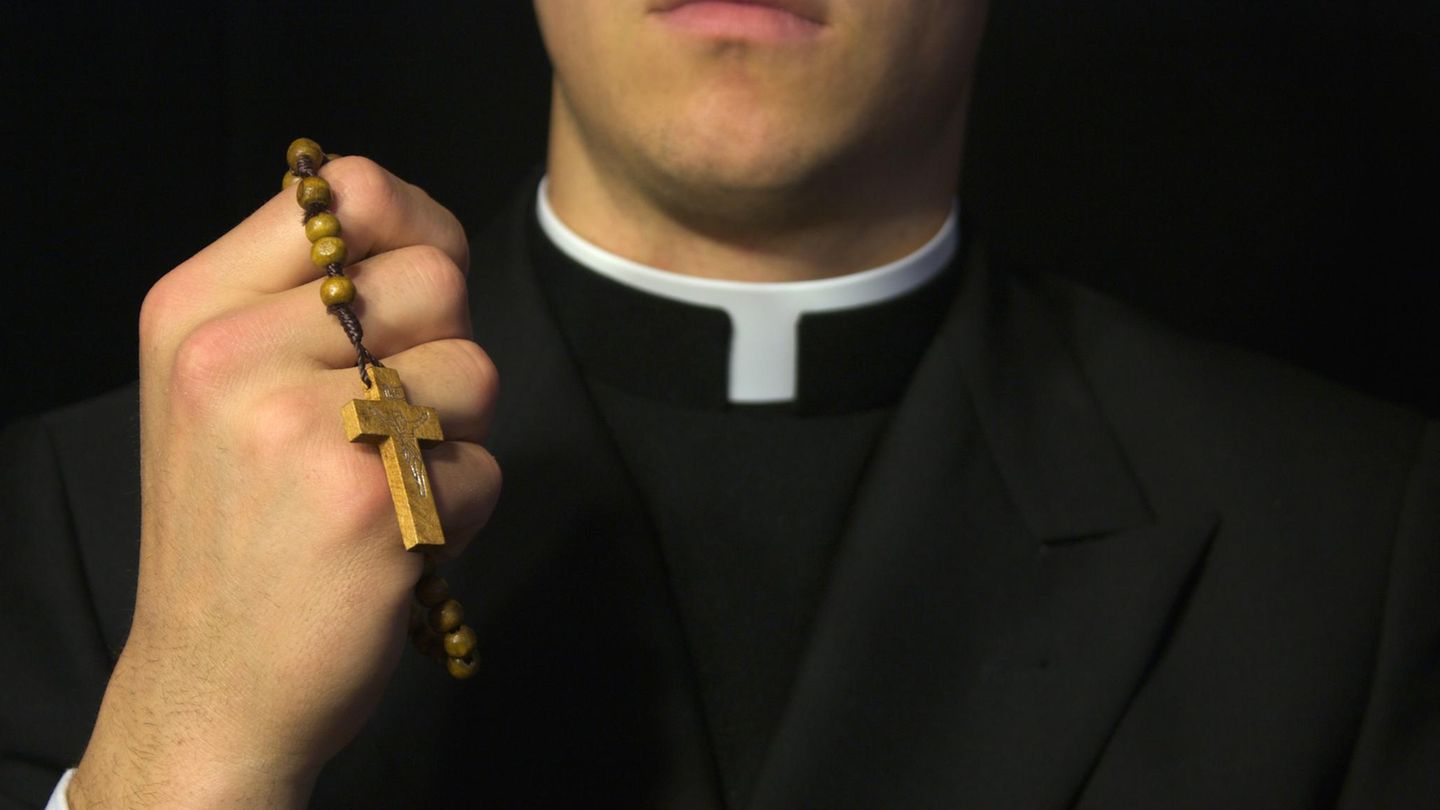 Ein katholischer Geistlicher hält einen Rosenkranz mit Kreuz
