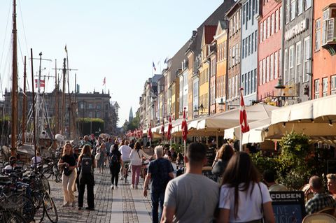 Passanten spazieren am Nyhavn in Kopenhagen entlang, dem bei Touristen beliebten Hafen mit seinen bunten Häuschen. 