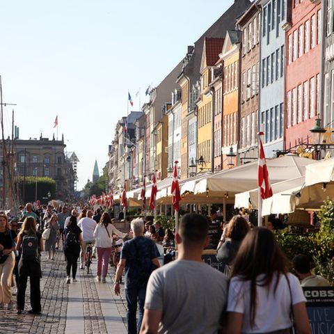 Passanten spazieren am Nyhavn in Kopenhagen entlang, dem bei Touristen beliebten Hafen mit seinen bunten Häuschen. 