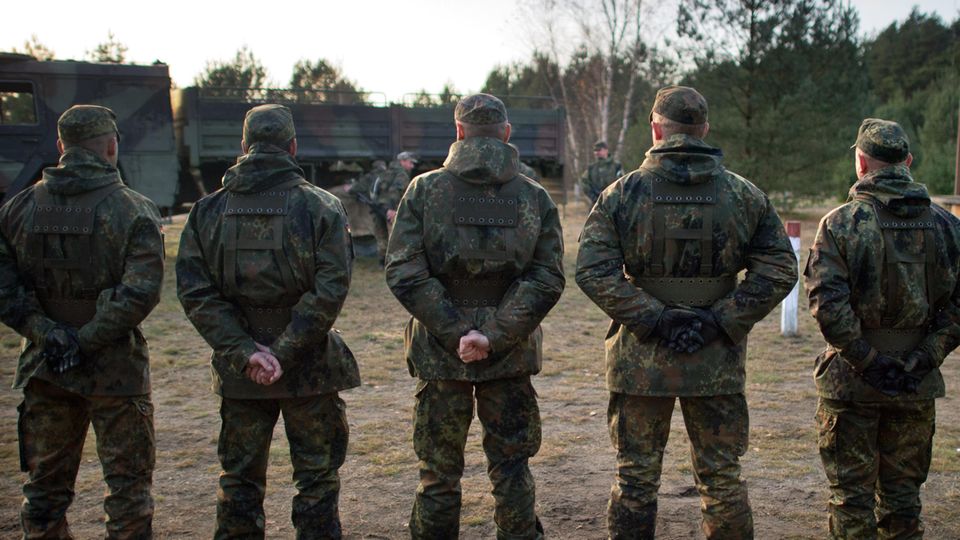 Von hinten sind fünf Bundeswehr-Soldaten zu sehen, die auf einem Truppenübungsplatz in einer Reihe stehen