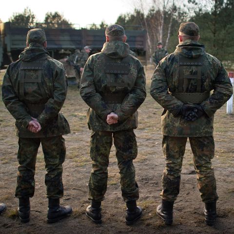 Von hinten sind fünf Bundeswehr-Soldaten zu sehen, die auf einem Truppenübungsplatz in einer Reihe stehen