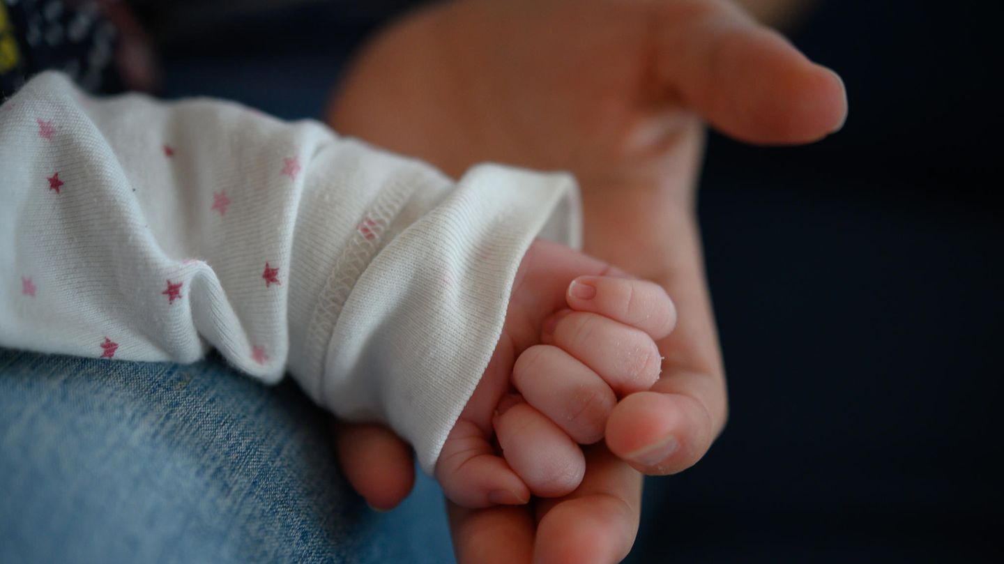 Die Hand eines zwei Wochen alten Neugeborenen liegt in der Hand seiner Mutter