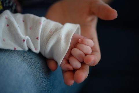Die Hand eines zwei Wochen alten Neugeborenen liegt in der Hand seiner Mutter